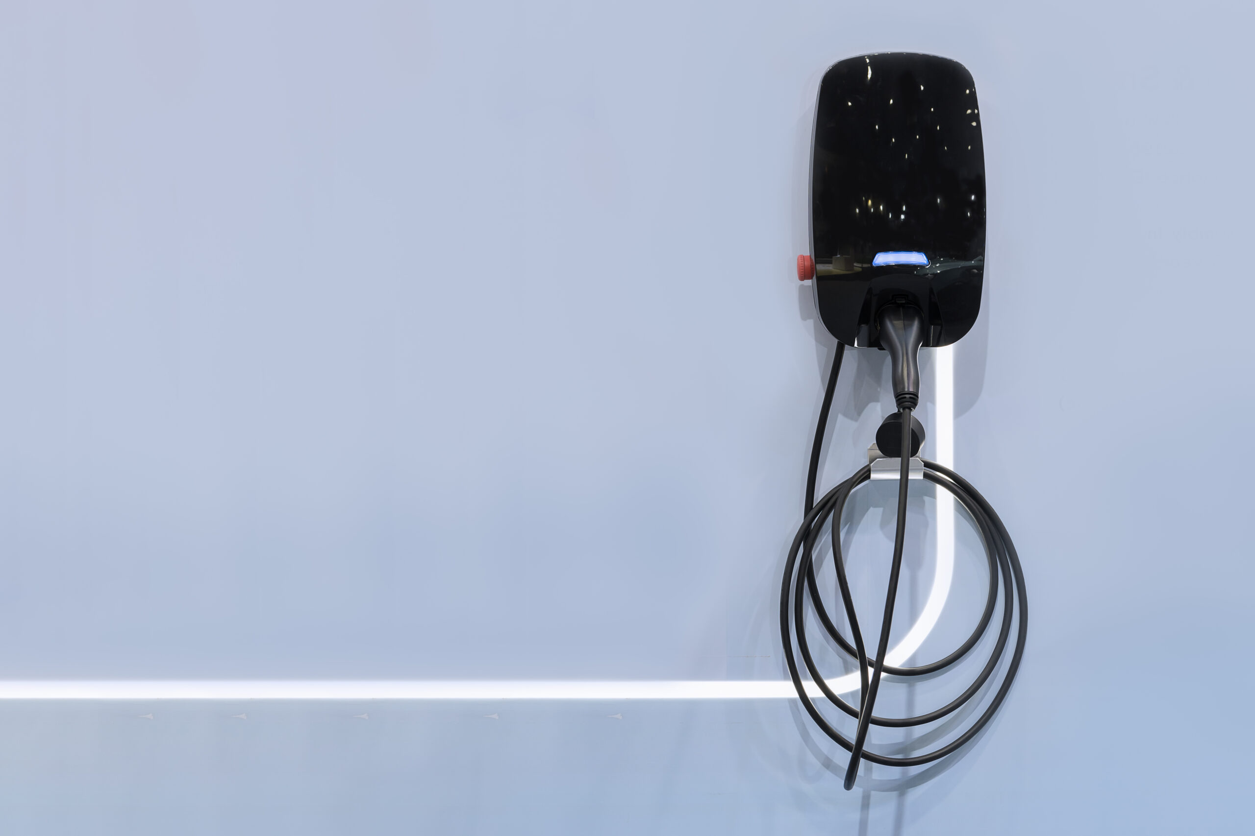 Electric vehicle wall charging station with black cable and connector, mounted on a light gray wall.